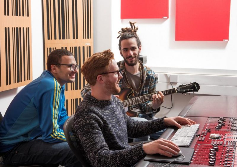 Musicians and producers learning in Abbey Road Institute Mixing Room with GIK Acoustics blonde 1D Alpha Corner Traps and red 242 Acoustic Panels squares behind the listening position